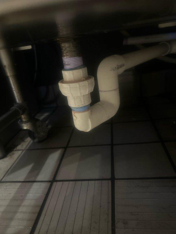 Responded to commercial water leak investigation at espresso machine and ice equipment area. Upon arrival, inspected plumbing connections beneath sink and equipment, identifying active leak at PVC union fitting connection on drain system that had been present for three days. Documented existing plumbing configuration including white PVC piping with threaded union assembly and surrounding commercial sink installation. Provided assessment and recommendations for repair to resolve ongoing water intrusion issue affecting commercial food service area.