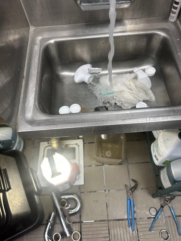 Responded to commercial water leak investigation at espresso machine and ice equipment area. Upon arrival, inspected plumbing connections beneath sink and equipment, identifying active leak at PVC union fitting connection on drain system that had been present for three days. Documented existing plumbing configuration including white PVC piping with threaded union assembly and surrounding commercial sink installation. Provided assessment and recommendations for repair to resolve ongoing water intrusion issue affecting commercial food service area.