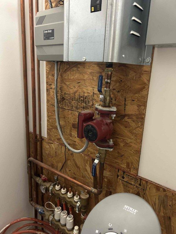 Responded to service call for kitchen sink drainage issue and malfunctioning garbage disposal producing humming noise. Diagnosed jammed garbage disposal impeller preventing proper operation and water drainage. Cleared obstruction from disposal unit and restored normal function. Additionally inspected radiant floor heating system per customer request regarding uneven heating in certain zones. Examined hydronic heating manifold, circulator pump, and zone valve actuators mounted on mechanical board. Identified potential issues with zone valve operation affecting heat distribution to specific floor areas. Documented heating system components including red circulator pump with brass fittings, multi-port brass manifold with white actuator controls, copper supply and return lines, PEX distribution tubing, expansion tank, and associated control equipment. System evaluation revealed possible actuator malfunction or air in lines contributing to inconsistent floor heating performance in affected 