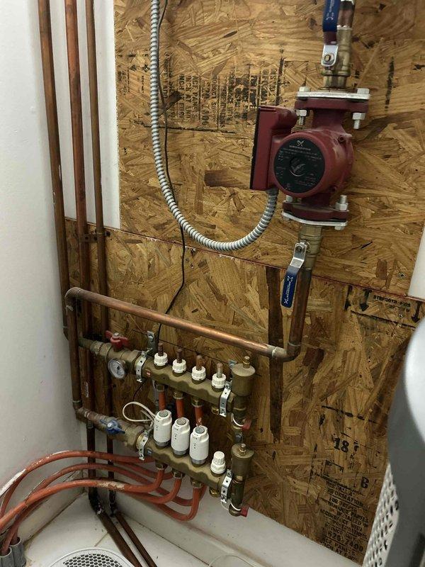 Responded to service call for kitchen sink drainage issue and malfunctioning garbage disposal producing humming noise. Diagnosed jammed garbage disposal impeller preventing proper operation and water drainage. Cleared obstruction from disposal unit and restored normal function. Additionally inspected radiant floor heating system per customer request regarding uneven heating in certain zones. Examined hydronic heating manifold, circulator pump, and zone valve actuators mounted on mechanical board. Identified potential issues with zone valve operation affecting heat distribution to specific floor areas. Documented heating system components including red circulator pump with brass fittings, multi-port brass manifold with white actuator controls, copper supply and return lines, PEX distribution tubing, expansion tank, and associated control equipment. System evaluation revealed possible actuator malfunction or air in lines contributing to inconsistent floor heating performance in affected 