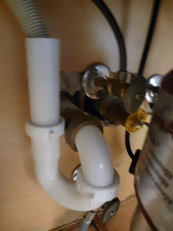 Responded to a clogged kitchen sink complaint and performed diagnostic inspection of the drainage system. Upon examination of the under-sink plumbing configuration, assessed the garbage disposal unit, P-trap assembly, and associated drain lines for blockages or mechanical failures. Documented existing plumbing conditions including the disposal unit with rubber splash guard, PVC drainage piping, corrugated drain hose connections, and trap configuration to identify the source of the stoppage and determine appropriate clearing methods.