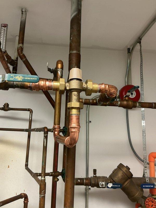 Installed a Watts tempering valve with 1" copper lead-free shut-off isolation valves to regulate water temperature in the existing tanked water heater system. The installation included proper integration with the existing copper pipe network, installation of brass fittings and control valves, and appropriate drain provisions. All work completed with 2-year parts warranty and lifetime workmanship guarantee.