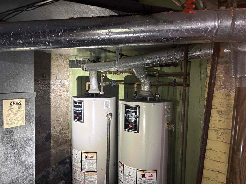 Conducted on-site evaluation for replacement of existing 40-gallon Bradford White gas water heater in basement mechanical room. Assessed current installation featuring dual water heater configuration with overhead gas piping, flexible ductwork, and venting system. Documented existing conditions including water heater placement, gas line connections, exhaust venting arrangements, and clearance requirements within unfinished basement space with concrete block walls and exposed structural elements. Provided estimate for removal of old unit and installation of new standard tank-style gas water heater with proper venting and code-compliant connections.