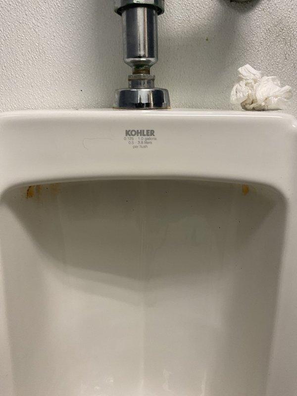 Responded to emergency dispatch for men's restroom urinal overflowing when flushed. Inspected Kohler wall-mounted urinal and flush valve assembly, identified malfunction in flush valve mechanism causing continuous water flow. Repaired flush valve hardware, tested operation to confirm proper flushing cycle without overflow, and placed facility back in service with caution signage removed.