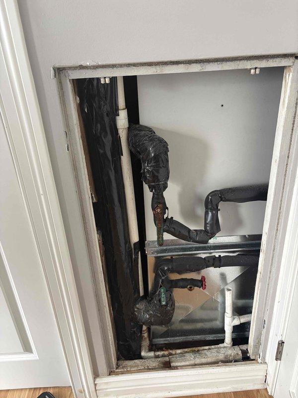 Conducted pre-repair assessment of two air handler units with severely corroded isolation valves. Accessed mechanical chase through wall panel to inspect HVAC piping system and document valve conditions. Evaluated scope of work required for valve replacement, which is scheduled to coincide with building-wide heating/cooling line drainage. Photographed existing conditions showing insulated refrigerant lines and valve locations within the mechanical access space. Provided detailed estimate for valve replacement work to be performed during the planned system shutdown window.