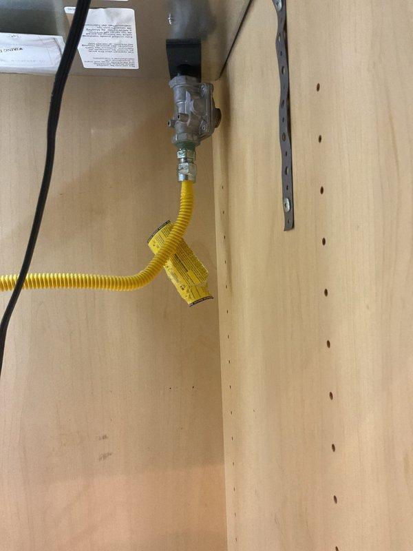 Installed gas pressure regulator and connected flexible CSST gas line to stove supply valve within utility cabinet. Verified proper valve operation and secure connections to ensure safe appliance functionality.
