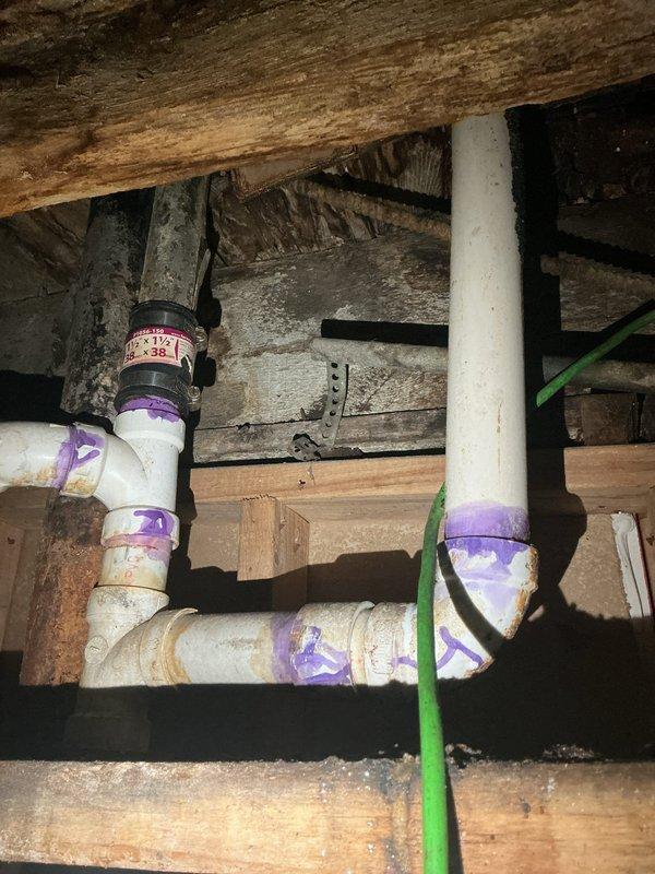 Completed bathroom re-pipe installation with new PVC piping system. Removed existing plumbing infrastructure and installed replacement supply lines and drain piping throughout the bathroom area, including proper connections at ceiling joists and structural framing members. All PVC joints were properly primed and solvent-welded per code requirements, with purple primer visible at all connection points to ensure quality assurance documentation.