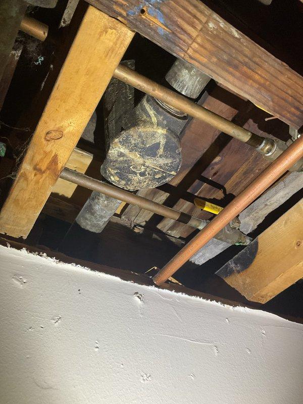 Responded to water leak in basement originating from exposed plumbing in ceiling below bathroom. Upon inspection, identified active leak from PVC pipe junction in floor framing system with clean water supply line affected. Documented existing plumbing configuration including PVC T-junction, copper supply lines, and cast iron components routed through floor joists and subfloor structure. Assessed leak source and determined water intrusion was from potable water supply system rather than wastewater drainage. Photographed affected plumbing connections and surrounding structural elements for documentation and further repair planning.