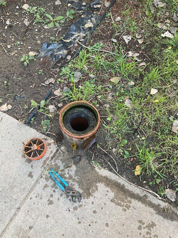 Responded to a residential sewer backup complaint with main line not draining properly. Upon arrival, located and accessed the exterior sewer cleanout near the foundation of the property. Inspection revealed a blockage in the main sewer line preventing proper drainage from the manhole connection. Documented the cleanout access point condition and surrounding area, noting the removal of the cleanout cover to assess the system. Provided estimate for necessary sewer line cleaning and blockage removal to restore proper drainage function.