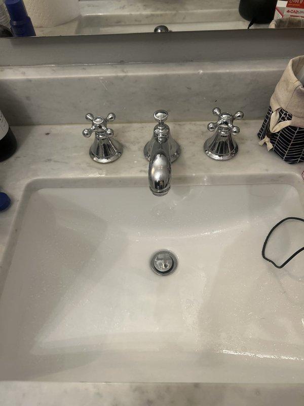 Replaced bathroom sink faucet assembly with new three-handle chrome fixture featuring separate hot and cold cross-handle taps and central spout. Installed new drain assembly and P-trap, connected supply lines to shut-off valves, and verified proper operation with no leaks detected.