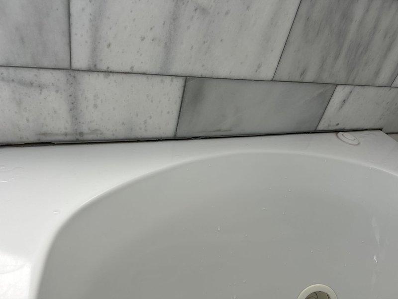 Responded to water intrusion complaint affecting dining room ceiling below master bathroom. Conducted visual inspection of master bathtub area and identified water staining on ceiling panels and surrounding tile surfaces. Recommended opening ceiling to access and identify leak source, followed by diagnostic testing of bathtub drain assembly and faucet connections to determine point of failure. Documented conditions with photographs showing discoloration patterns on ceiling panels and tile surfaces adjacent to tub fixture. Advised client that additional repair recommendations and estimates would be provided upon completion of diagnostic work and leak source identification.