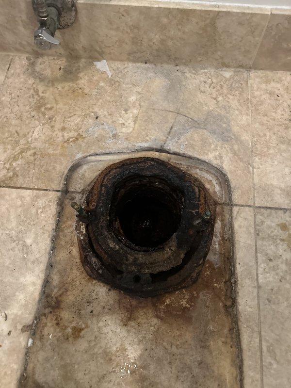 Responded to water leak investigation request from property below affected unit. Conducted visual inspection of bathroom floor drain and surrounding area to assess potential leak source. Documented heavily corroded floor drain fixture with extensive rust deterioration and mineral deposit accumulation on metal rim and interior surfaces. Observed significant water staining and discoloration patterns radiating outward from drain on tile flooring, indicating prolonged moisture exposure. Photographed corroded drain assembly and deteriorated grout lines for estimate preparation. Identified aged plumbing fixture requiring replacement due to advanced corrosion compromising drain integrity. Coordinated with upstairs residents to schedule follow-up estimate for necessary repairs.