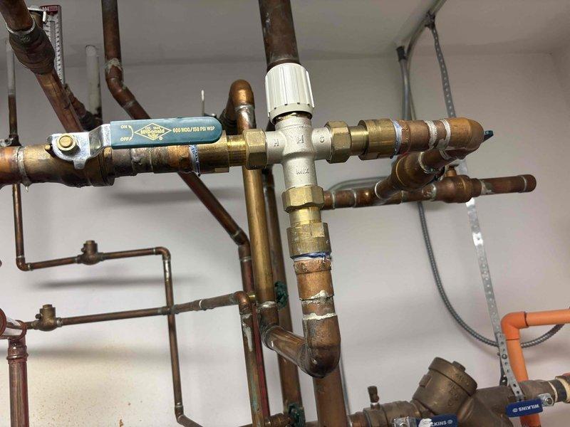 Responded to service call for significant loss of hot water throughout the home. Upon arrival, confirmed hot water was present at the tank and valve but only lukewarm or unavailable at multiple fixtures including shower. Inspected the indirect-fired water heating system and complex copper piping network. Diagnosed faulty thermostatic mixing valve assembly causing inadequate hot water distribution to fixtures. The mixing valve was failing to properly blend hot and cold water, resulting in insufficient hot water delivery despite proper tank operation. Adjusted and tested the mixing valve control to restore proper temperature balance. Verified hot water temperature and flow at all affected fixtures including shower. System returned to normal operation with adequate hot water supply throughout the home.