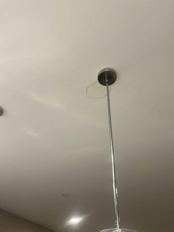 Responded to plumbing service call for ceiling-mounted light fixture installation or repair. Upon arrival, accessed ceiling penetration point where fixture pole extends through drywall. Masked off work area with painter's tape in crosshatch pattern to protect surrounding ceiling surface during repair work. Secured pendant light fixture with chrome mounting canopy at ceiling junction, ensuring proper alignment and stability of extended pole assembly. Completed installation with fixture properly mounted and operational alongside existing recessed lighting.