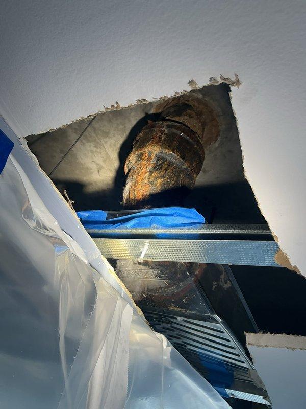 Responded to water intrusion concerns and conducted thorough plumbing inspection of exposed piping system through ceiling access point. Upon arrival, homeowner had already opened ceiling to investigate water staining and requested detailed assessment of plumbing infrastructure condition.

Inspection revealed severely corroded cast iron pipe system with extensive deterioration throughout visible sections. Primary findings included a 90-degree elbow joint exhibiting advanced rust coverage with orange, brown, and black corrosion patterns across entire surface. Metal showed significant flaking, surface degradation, and complete failure of original protective coating in multiple areas. Corrosion was most pronounced on curved elbow section where metal substrate was exposed beneath deteriorated coating layers.

Additional piping visible through ceiling opening displayed similar rust patterns and surface deterioration, indicating systemic corrosion issues rather than isolated failure. The adva