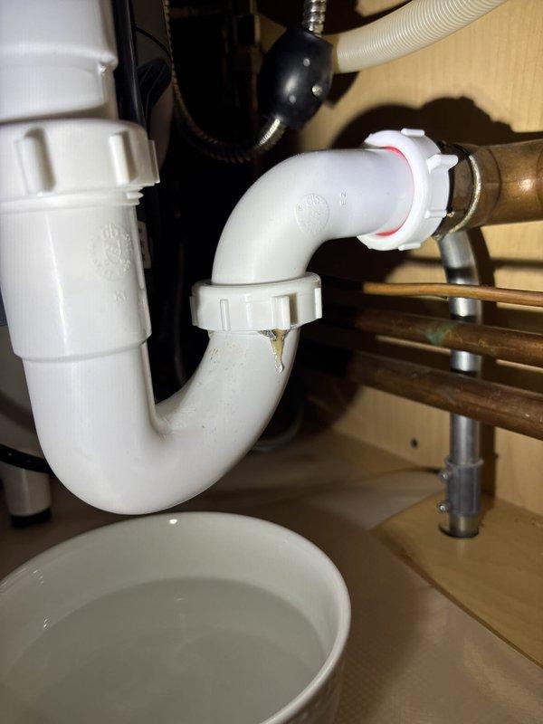 Responded to a leak under the kitchen sink. Upon inspection, identified moisture at the P-trap connection and disposal discharge assembly. Tightened compression fittings on the white PVC P-trap where it connects to the copper tailpiece, ensuring proper seal with the red rubber gasket. Verified all connections between the garbage disposal unit and drain assembly were secure. Tested system by running water through the sink and disposal unit, confirming no leaks present at any connection points.