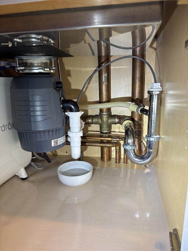 Responded to a leak under the kitchen sink. Upon inspection, identified moisture at the P-trap connection and disposal discharge assembly. Tightened compression fittings on the white PVC P-trap where it connects to the copper tailpiece, ensuring proper seal with the red rubber gasket. Verified all connections between the garbage disposal unit and drain assembly were secure. Tested system by running water through the sink and disposal unit, confirming no leaks present at any connection points.