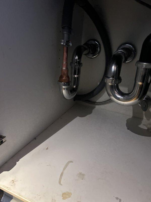 Responded to water leak locate service call for plumbing fixture. Upon inspection, identified corrosion and oxidation on chrome P-trap assembly beneath sink, with visible brown/copper-colored discoloration on vertical section near wall connection. Documented existing conditions showing signs of deterioration on left drain pipe and staining on cabinet base surface. Photographed affected plumbing connections and replacement P-trap components for service records.