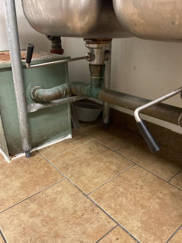 Responded to commercial kitchen plumbing service call where inspection revealed significant corrosion on utility infrastructure and mechanical systems. Documented deteriorated conditions including heavily rusted step platform beneath commercial sink area and corroded valve fittings on suspended tank piping system in mechanical room. Assessed oxidized galvanized steel pipes, weathered connection points, and aging plumbing components showing mineral deposits and advanced corrosion throughout the installation.