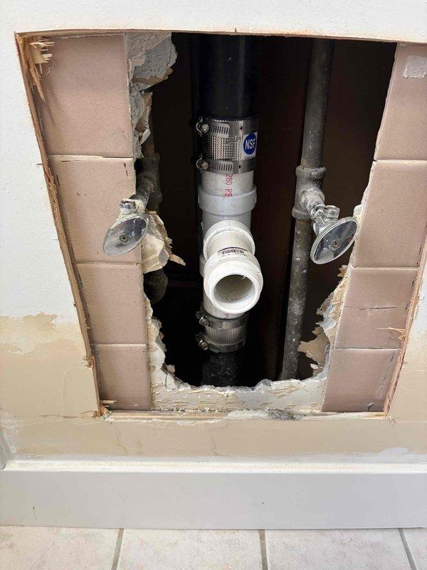 Performed plumbing repair requiring wall access to address drain line issues. Cut access opening in tiled wall to expose defective PVC drain pipe assembly. Replaced damaged sections of vertical drain line using new PVC pipe, flexible fernco couplings, and stainless steel hose clamps to ensure proper watertight connections. Verified all connections were secure and properly aligned with existing plumbing infrastructure.