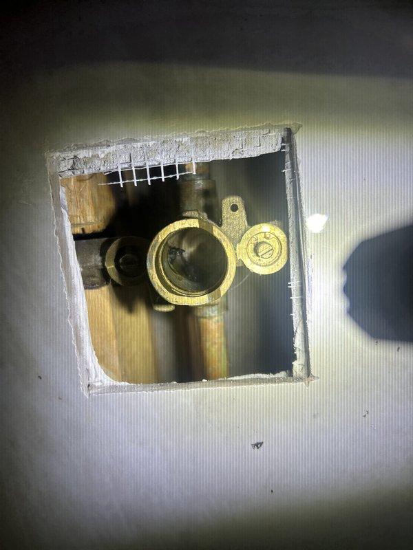 Responded to water leak complaint originating from shower head assembly. Upon inspection, identified faulty connection at the shower valve body behind the wall. Created access opening in wall to expose plumbing infrastructure and brass valve assembly. Tightened mounting connections, inspected shower control valve and showerhead for proper seal integrity, and verified all fixtures were properly secured to eliminate leak source. Completed repairs and confirmed water flow operates without leakage.