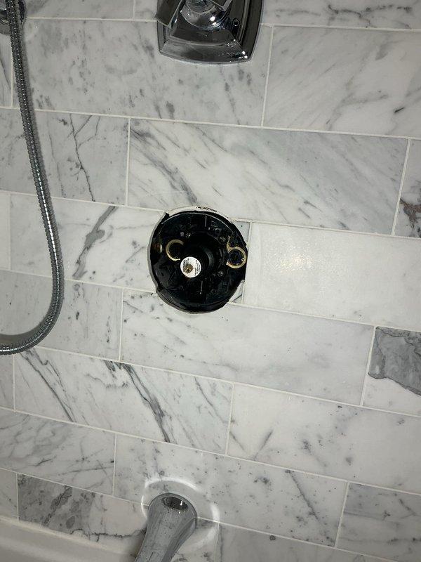 Completed installation of new shower fixtures in bathroom including chrome shower valve with cross-handle control, showerhead, handheld shower with flexible hose, and tub spout. All fixtures were mounted on newly installed white and gray marble-patterned tile work, with proper sealing and alignment to ensure leak-free operation.