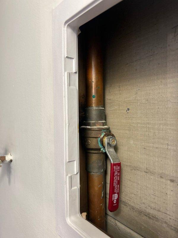 Conducted on-site plumbing assessment for malfunctioning shut-off valve that could not be turned off, requiring building water shutdown from 8AM-12PM. Inspected copper pipe installation with existing ball valve featuring deteriorated operation, documented condition showing age-related corrosion and patina on copper piping. Evaluated under-sink plumbing configuration including garbage disposal unit installation and associated drain connections. Provided estimate for shut-off valve replacement with no immediate work authorization requested.