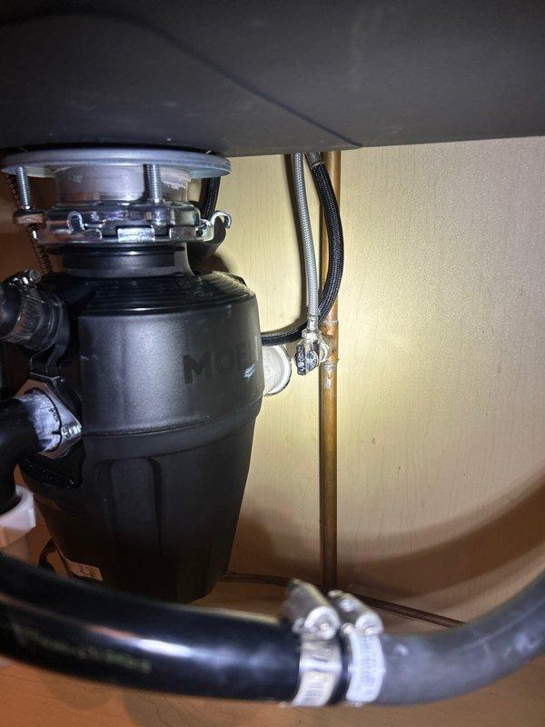 Conducted on-site plumbing assessment for malfunctioning shut-off valve that could not be turned off, requiring building water shutdown from 8AM-12PM. Inspected copper pipe installation with existing ball valve featuring deteriorated operation, documented condition showing age-related corrosion and patina on copper piping. Evaluated under-sink plumbing configuration including garbage disposal unit installation and associated drain connections. Provided estimate for shut-off valve replacement with no immediate work authorization requested.