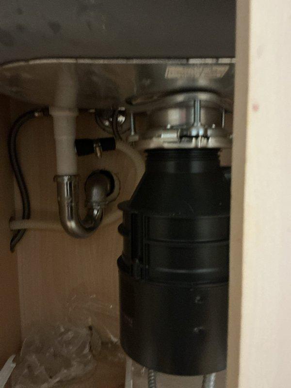Responded to a kitchen sink drainage issue and garbage disposal installation request. Successfully installed a new black garbage disposal unit under the kitchen sink, securing it with proper mounting hardware and metal ring assembly. Connected the disposal to the existing chrome P-trap drainage system and verified all connections were secure and leak-free. Tested the system to ensure proper drainage and confirmed the garbage disposal was functioning correctly.
