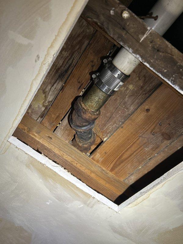 Responded to warranty call for recurring drainage backup issue. Inspected accessible plumbing system including overhead drain lines visible through ceiling access point and basement mechanical room infrastructure. Examined cast iron drain assembly with transition coupling to PVC piping at structural access opening, noting age-related corrosion on metal components. Assessed main plumbing distribution system in basement area including water heater connections and overhead insulated supply lines. Documented existing plumbing configuration and condition of drainage system components to verify previous service work and determine cause of ongoing backup concerns.
