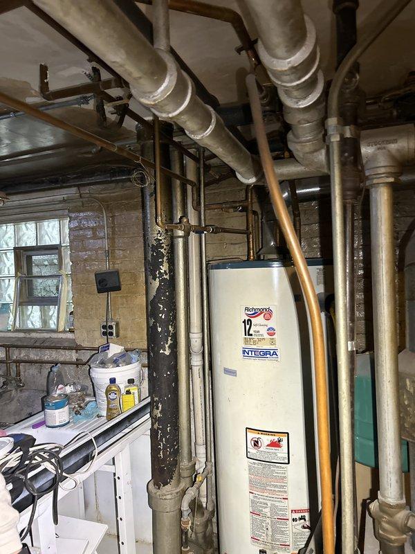 Responded to warranty call for recurring drainage backup issue. Inspected accessible plumbing system including overhead drain lines visible through ceiling access point and basement mechanical room infrastructure. Examined cast iron drain assembly with transition coupling to PVC piping at structural access opening, noting age-related corrosion on metal components. Assessed main plumbing distribution system in basement area including water heater connections and overhead insulated supply lines. Documented existing plumbing configuration and condition of drainage system components to verify previous service work and determine cause of ongoing backup concerns.