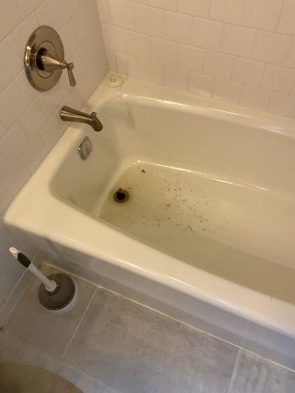 # Plumbing Service - Clogged Drain/Sink

Responded to clogged bathtub drain with slow drainage and visible debris accumulation. Upon inspection, found significant buildup of hair, soap residue, and foreign material obstructing the drain stopper mechanism and trap assembly. Removed chrome drain stopper assembly and extracted accumulated debris from the drain opening. Cleared blockage using appropriate drain cleaning tools and restored proper water flow. Tested drainage to confirm complete resolution of the clog. Additionally, inspected deteriorated cast iron drain pipe penetration in basement utility area showing advanced corrosion, rust staining, and compromised wall integrity with moisture damage to surrounding building materials, recommending future repair or replacement to prevent potential leaks and further structural deterioration.
