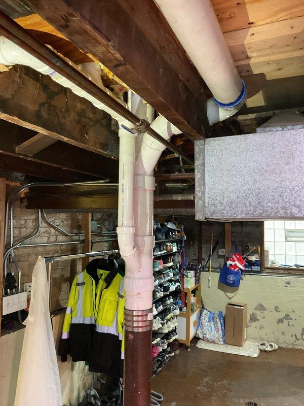 Collected down payment for upcoming plumbing repair work in basement utility area. Documented existing conditions including vertical PVC drainage pipe system with visible connections and couplings, exposed ceiling joists, and unfinished storage space requiring future service work.