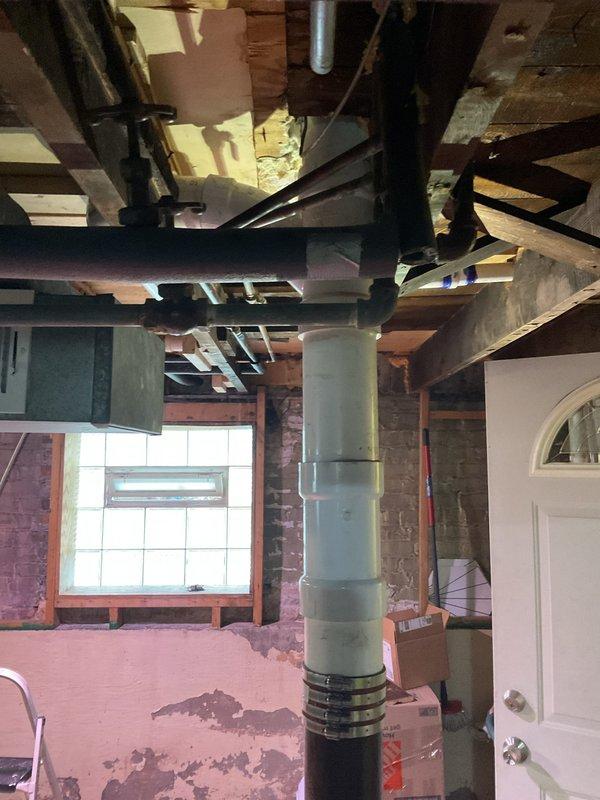 Collected down payment for upcoming plumbing repair work in basement utility area. Documented existing conditions including vertical PVC drainage pipe system with visible connections and couplings, exposed ceiling joists, and unfinished storage space requiring future service work.