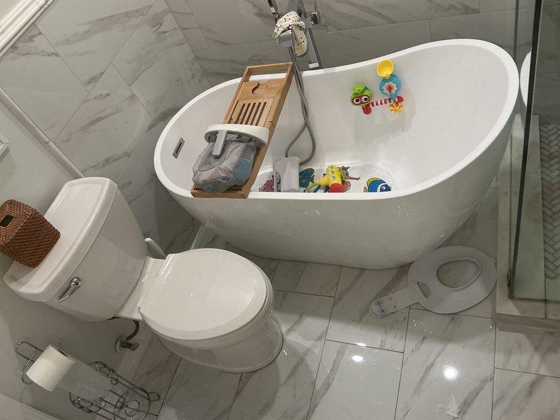 Completed plumbing service consultation for bathroom fixtures in modern residential setting. Assessed existing installation including freestanding oval bathtub, wall-mounted toilet, undermount vanity sink with contemporary black faucet, and frameless glass shower enclosure with handheld fixture and recessed storage niche. All fixtures evaluated for proper function and identified repair recommendations, with photographic documentation captured for service records.