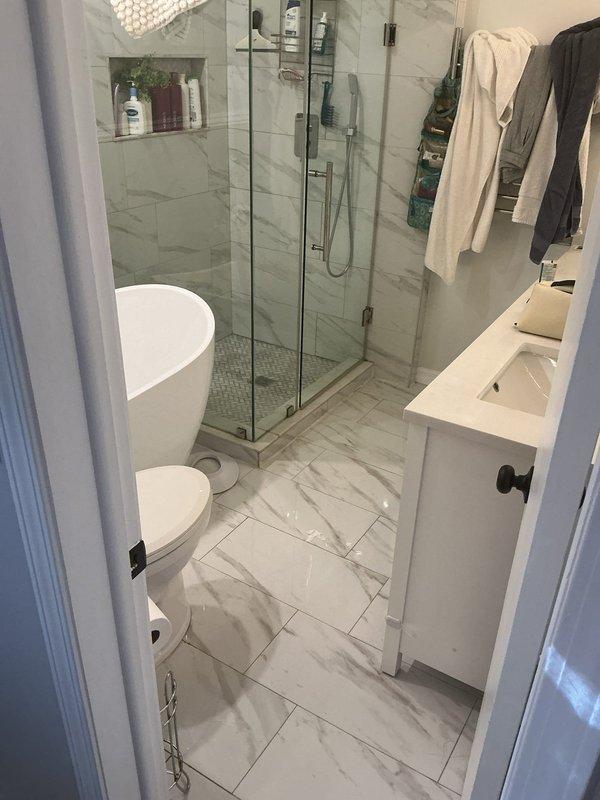 Completed plumbing service consultation for bathroom fixtures in modern residential setting. Assessed existing installation including freestanding oval bathtub, wall-mounted toilet, undermount vanity sink with contemporary black faucet, and frameless glass shower enclosure with handheld fixture and recessed storage niche. All fixtures evaluated for proper function and identified repair recommendations, with photographic documentation captured for service records.