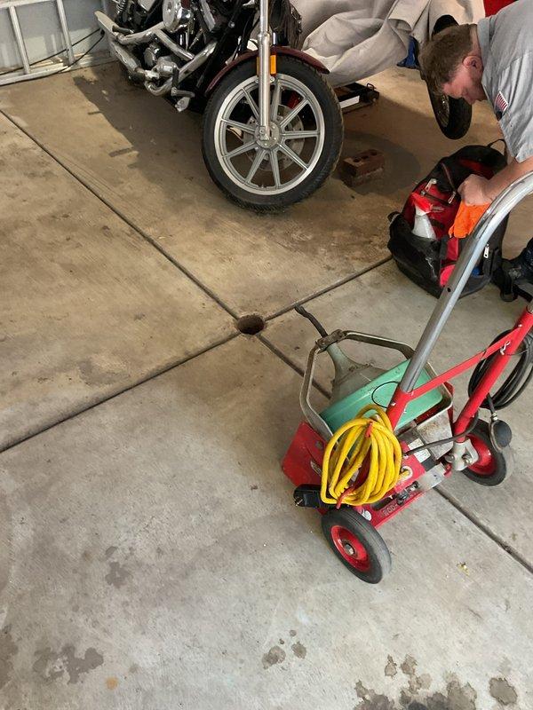 Responded to slow drain complaint at residential property. Upon arrival, located floor drain in garage area and performed inspection of drainage system. Utilized professional drain cleaning equipment, including pressure washing apparatus with hose assembly, to clear obstruction and restore proper flow. Verified drainage functionality upon completion of cleaning procedure.