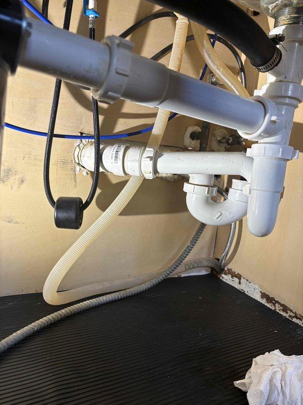 Responded to service call for reported leak under kitchen sink. Upon arrival, conducted thorough inspection of under-sink plumbing assembly including white PVC P-trap, drain connections, water supply lines, and garbage disposal connections. Identified source of leak at P-trap connection point. Disassembled affected P-trap assembly, inspected washers and seals for deterioration, and cleaned all mating surfaces. Reinstalled P-trap with proper alignment and hand-tightened connections to manufacturer specifications. Verified all supply line connections, hose clamps, and flexible drain hoses were secure. Conducted water flow test by running both hot and cold water through sink drain while monitoring all connections for leaks. Confirmed repair was successful with no active leaking present. Documented plumbing configuration with photos showing completed installation and proper drainage assembly.