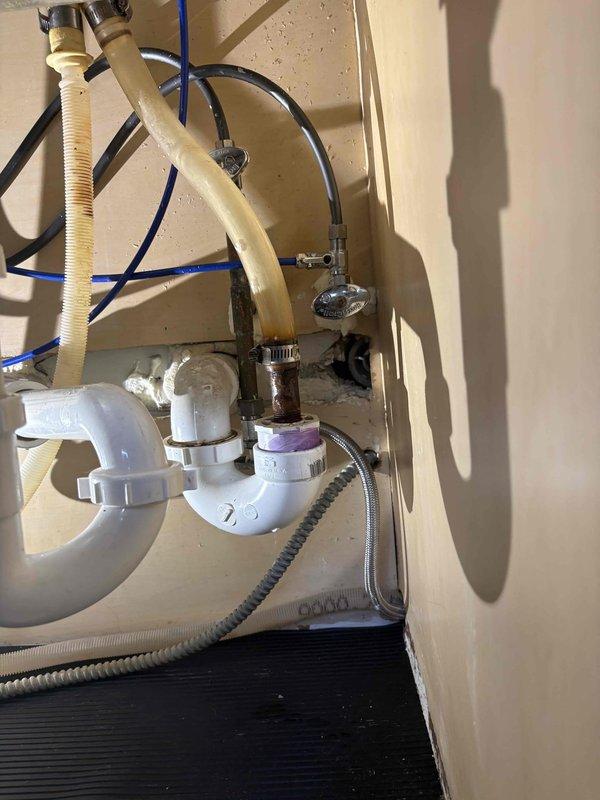 Responded to service call for reported leak under kitchen sink. Upon arrival, conducted thorough inspection of under-sink plumbing assembly including white PVC P-trap, drain connections, water supply lines, and garbage disposal connections. Identified source of leak at P-trap connection point. Disassembled affected P-trap assembly, inspected washers and seals for deterioration, and cleaned all mating surfaces. Reinstalled P-trap with proper alignment and hand-tightened connections to manufacturer specifications. Verified all supply line connections, hose clamps, and flexible drain hoses were secure. Conducted water flow test by running both hot and cold water through sink drain while monitoring all connections for leaks. Confirmed repair was successful with no active leaking present. Documented plumbing configuration with photos showing completed installation and proper drainage assembly.