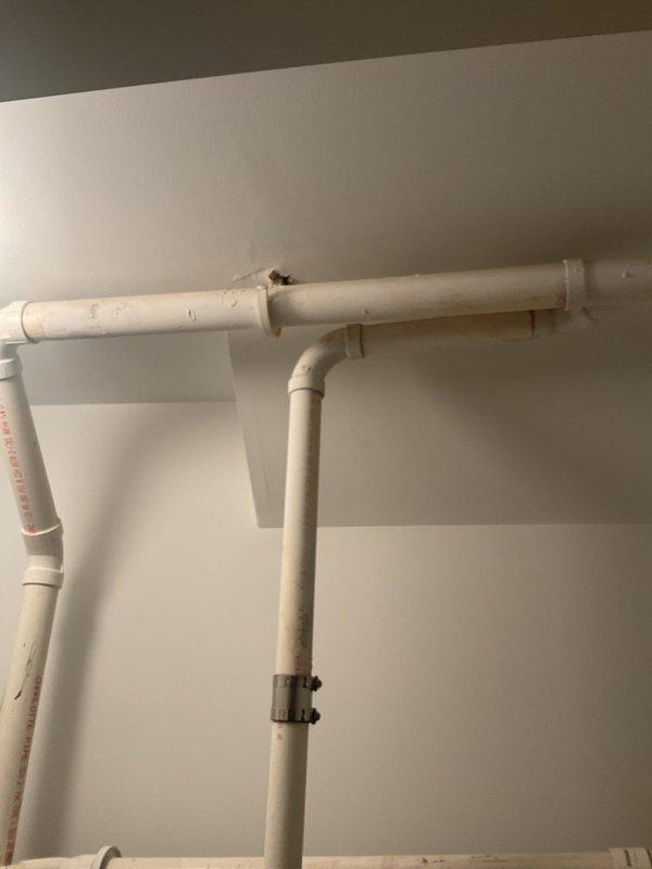 Responded to service call for residential ejector pump reported as not cycling. Performed diagnostic inspection of the sump pump system located in basement utility area. Assessed pump basin, discharge piping configuration including white PVC vertical and horizontal runs, electrical connections, and standing water level in basin. Documented existing plumbing installation with photos showing pump basin with cover displaced, dual vertical PVC discharge pipes, wall-mounted water heater with associated plumbing connections, and electrical supply components including outlet and transformer. Explained that replacement cost estimates would be provided on-site following complete system evaluation.