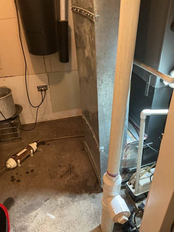 Responded to service call for tankless water heater that developed a leak following scheduled maintenance visit. Upon arrival, inspected white wall-mounted tankless unit and associated copper supply piping for source of water intrusion. Identified active leak condition requiring immediate attention. Placed collection bucket beneath unit to capture water discharge and prevent further damage to basement utility area. Documented equipment condition and leak location with photographs showing tankless heater installation, surrounding plumbing connections, PVC drainage system, and floor moisture patterns. Unit is a 2022 model requiring further diagnostic evaluation and repair to resolve leak issue and restore proper operation.