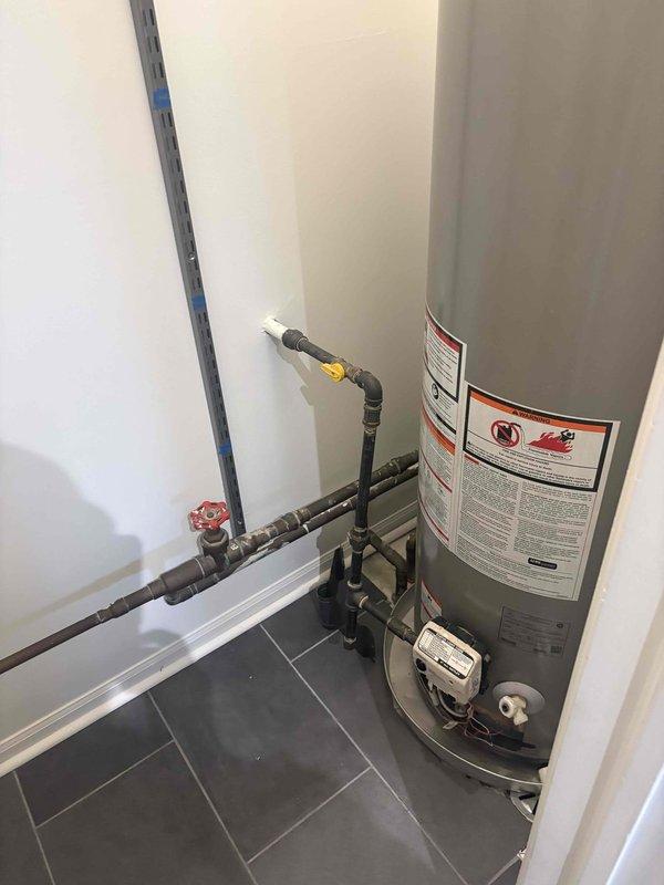 Responded to no hot water complaint on newly installed tank water heater in basement. Upon arrival, inspected unit and discovered power supply issue preventing heater operation. Verified all plumbing connections, including copper supply lines with foam insulation, galvanized vent piping, and PVC discharge line were properly installed and secure. Checked temperature and pressure relief valve functionality and confirmed proper venting configuration. Restored power to unit, verified pilot light ignition system engaged correctly, and confirmed burner assembly fired properly. Tested hot water flow at fixtures throughout home and verified system reached target temperature. All safety labels and warning stickers present and legible on tank exterior. Unit returned to full operational status with hot water restored.