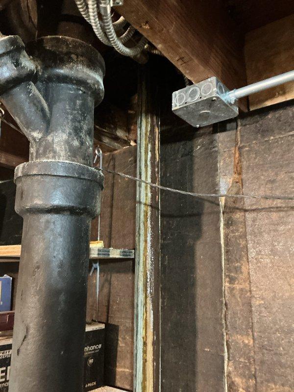 Performed a water leak locate investigation for a reported upstairs bathtub leak migrating through the downstairs wall cavity to the basement drain line. Inspected the kitchen ceiling and cabinetry below the bathroom, finding no visible staining or moisture damage, then examined the basement cast iron drain stack, including the Y-branch fitting and coupling band, along with adjacent framing, where discoloration and mineral residue were noted as evidence of prior or ongoing moisture migration. Documented findings with photos to support further diagnosis and repair of the bathtub drain/overflow assembly or connected drain piping.
