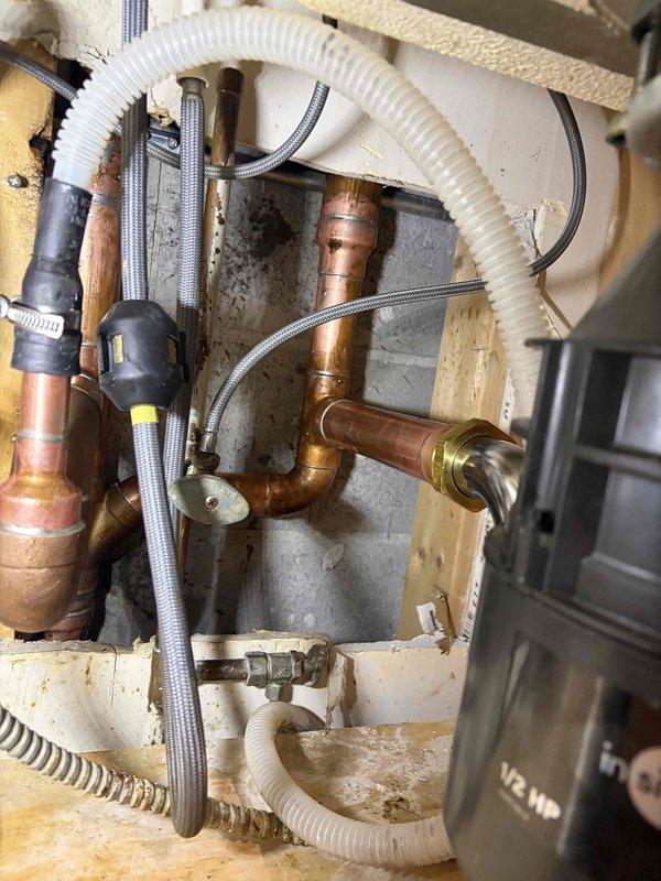 Performed plumbing repair at the kitchen sink, accessing the under-sink cavity and the wall cutout to service the copper supply lines, soldered joints, and fittings. Inspected and repaired the copper piping and connections, then verified the shutoff valve, braided flexible supply line, and chrome P-trap drain assembly were properly seated and secure, with the garbage disposal connection left intact.