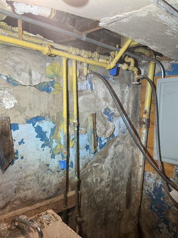 Found the 1 1/2" cast iron first-floor kitchen drain corroded through at its connection to the 6" clay and concrete line, so the drain was rerouted into the 4" toilet stack. After securing the cast iron stack to adjacent framing with band iron, a section was removed and replaced with new 4" PVC including a 4"x2" wye, and the old kitchen drain was removed and the abandoned opening sealed with hydraulic cement. A new 2" PVC kitchen drain was then run through the open joist space along the air duct to the new wye and strapped securely.