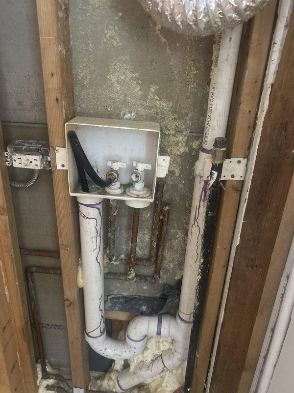 Performed a plumbing repair within the open wall cavity at the recessed washing machine outlet box, working during a scheduled building shutdown. Serviced the washer supply valves and associated brass fittings, and addressed the Schedule 40 PVC drain assembly, including the P-trap and vertical drain connections secured to the framing. Inspected the adjacent corroded copper supply lines, completed primed and cemented PVC joints, and left the system properly connected and supported.