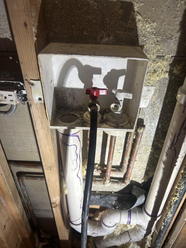 Performed a plumbing repair within the open wall cavity at the recessed washing machine outlet box, working during a scheduled building shutdown. Serviced the washer supply valves and associated brass fittings, and addressed the Schedule 40 PVC drain assembly, including the P-trap and vertical drain connections secured to the framing. Inspected the adjacent corroded copper supply lines, completed primed and cemented PVC joints, and left the system properly connected and supported.