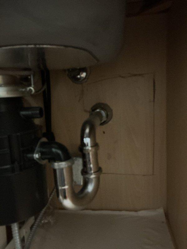 Serviced and tightened the chrome P-trap drain assembly at the bathroom sink using a pipe wrench on the slip nut connection, and inspected the adjacent braided supply lines and shut-off valves. Also inspected the kitchen sink drain assembly, including the garbage disposal discharge elbow and P-trap connection to the wall. All connections were confirmed secure, with no leaks, rust, or corrosion observed.