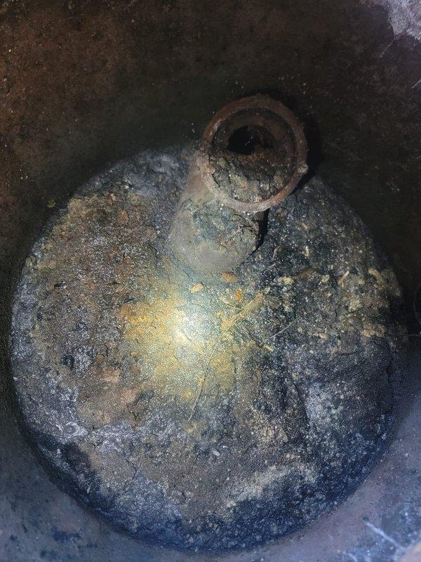 Inspected the shared grease trap serving six units and found heavy accumulation of grease, sludge, and sediment, along with significant corrosion on the inlet pipe stub and deteriorating concrete along the interior walls. Documented the condition with photographs and recommended pumping and cleaning of the trap, along with repair or replacement of the corroded inlet piping, to restore proper drainage and prevent recurring backups.