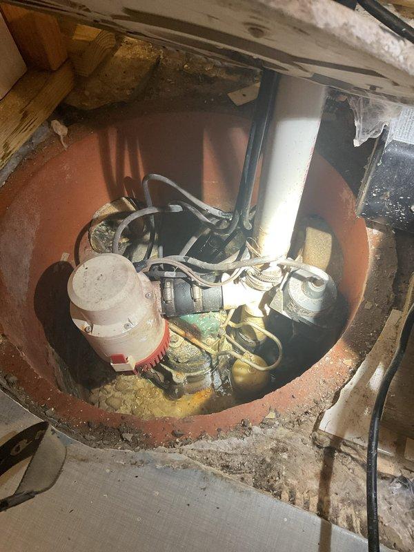 Performed an on-site estimate for replacement of the failed primary and battery backup sump pumps. Inspection of the sump pit found a corroded submersible pump and secondary pump or float assembly, sediment buildup, and a PVC discharge line with check valve, along with a Basement Defender backup control and charging system on the adjacent wall. Documented system conditions with photos and provided recommendations for pump replacement; no repairs were performed at this time per the customer's request.